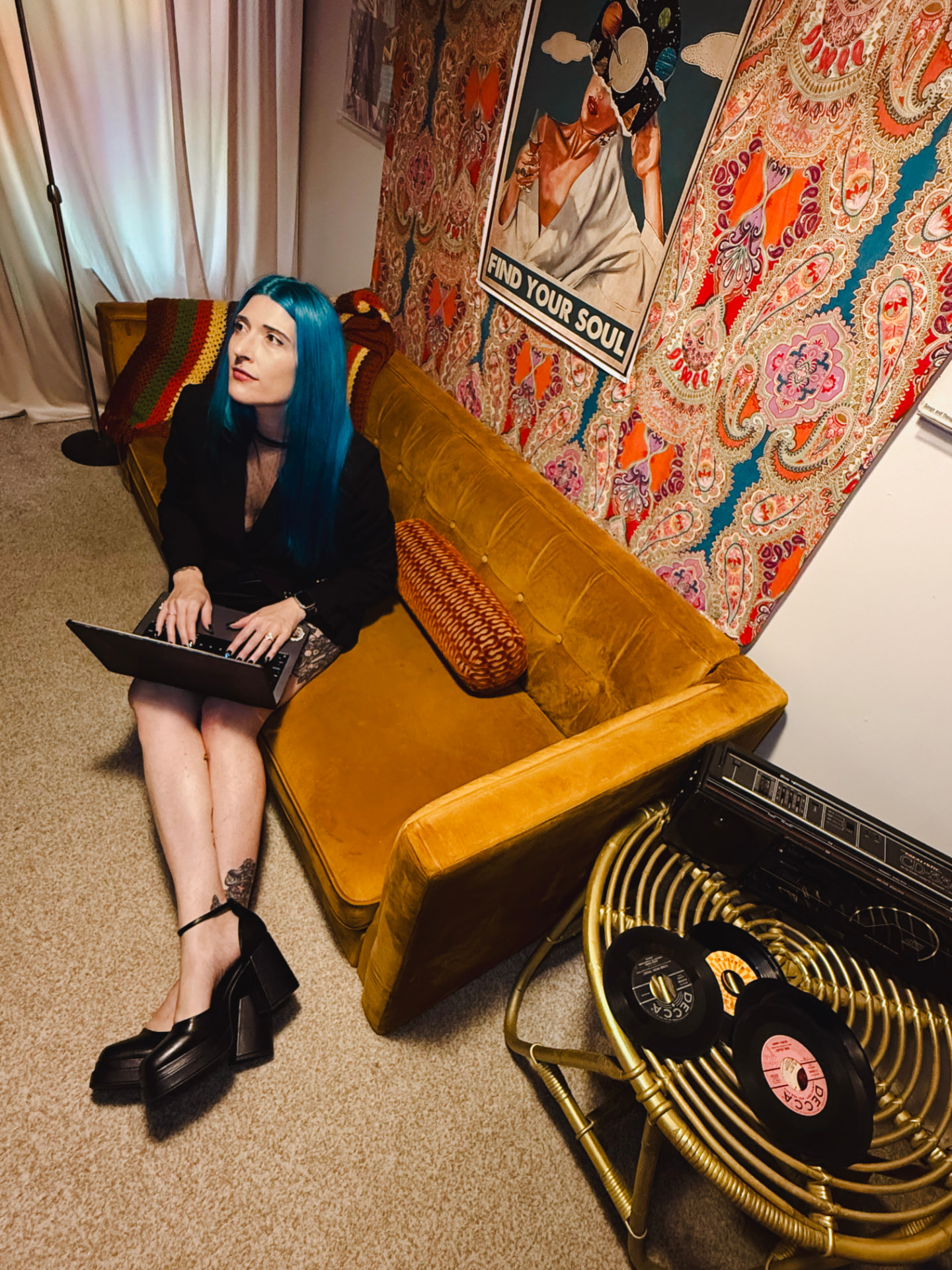 Amanda seated on a gold velvet sofa with an open laptop, looking up in thought